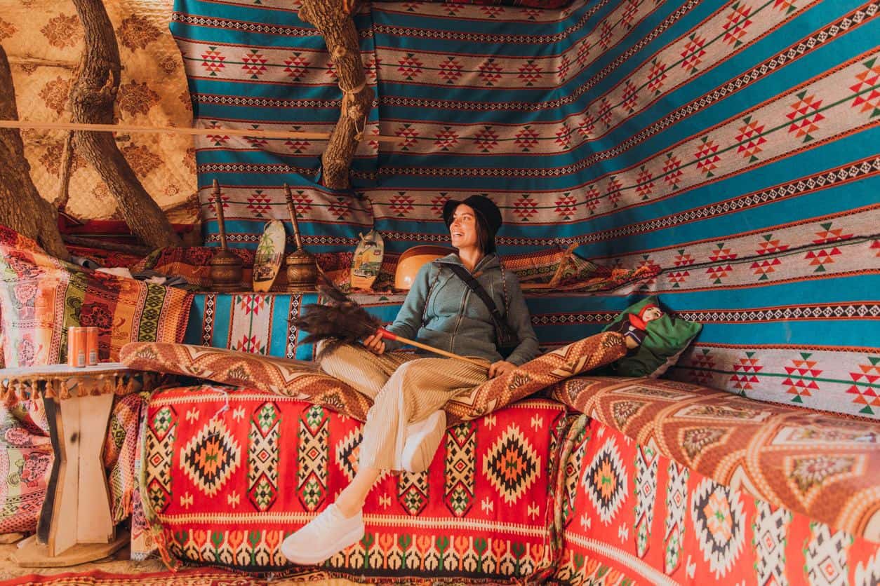 Traveler relaxing inside a traditional Bedouin tent in Jordan, surrounded by colorful woven textiles and desert camp decor