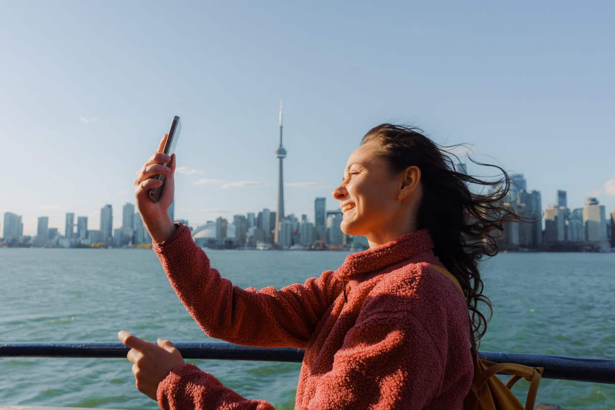 Traveler smiling and taking a photo with the Toronto skyline in the background along the waterfront