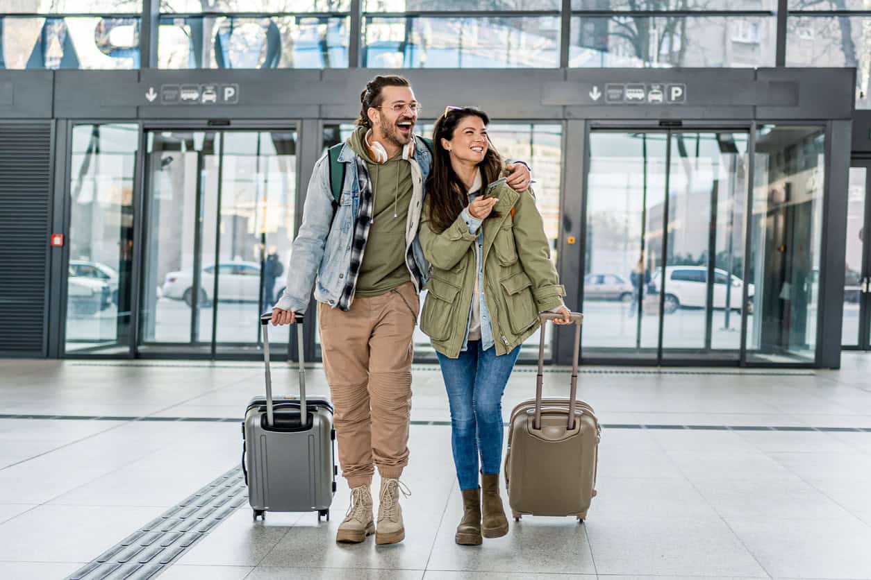 Couple walking through airport terminal with carry-on luggage ready for travel departure