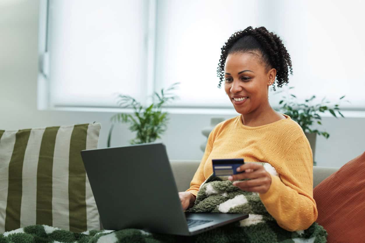 Woman sitting on a couch using a credit card and laptop to book flights or travel online