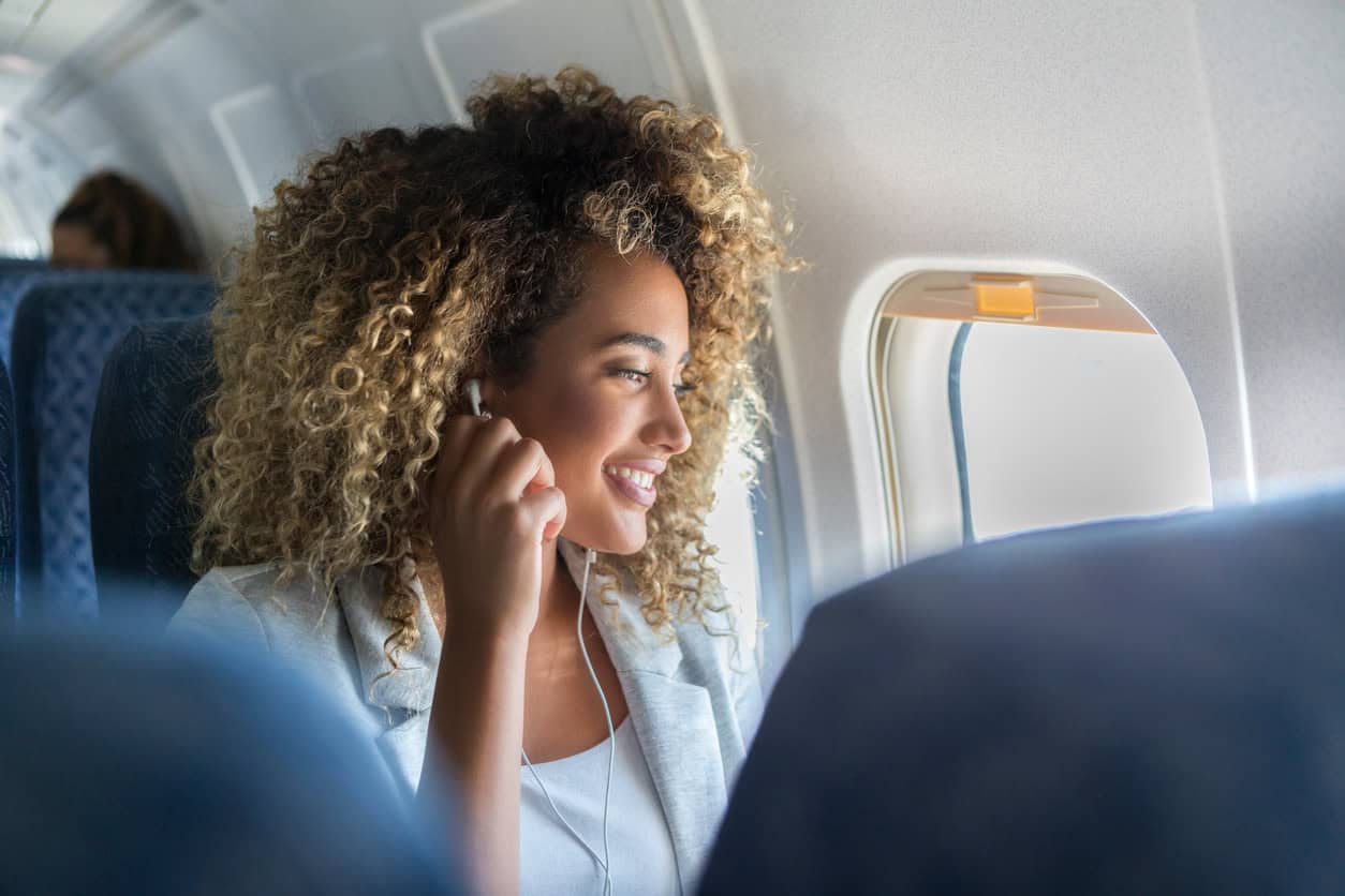 Woman wearing earphones and smiling while looking out the airplane window during a flight