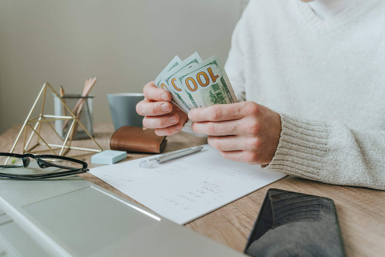 Person counting cash at a desk while reviewing rent payments and managing monthly expenses