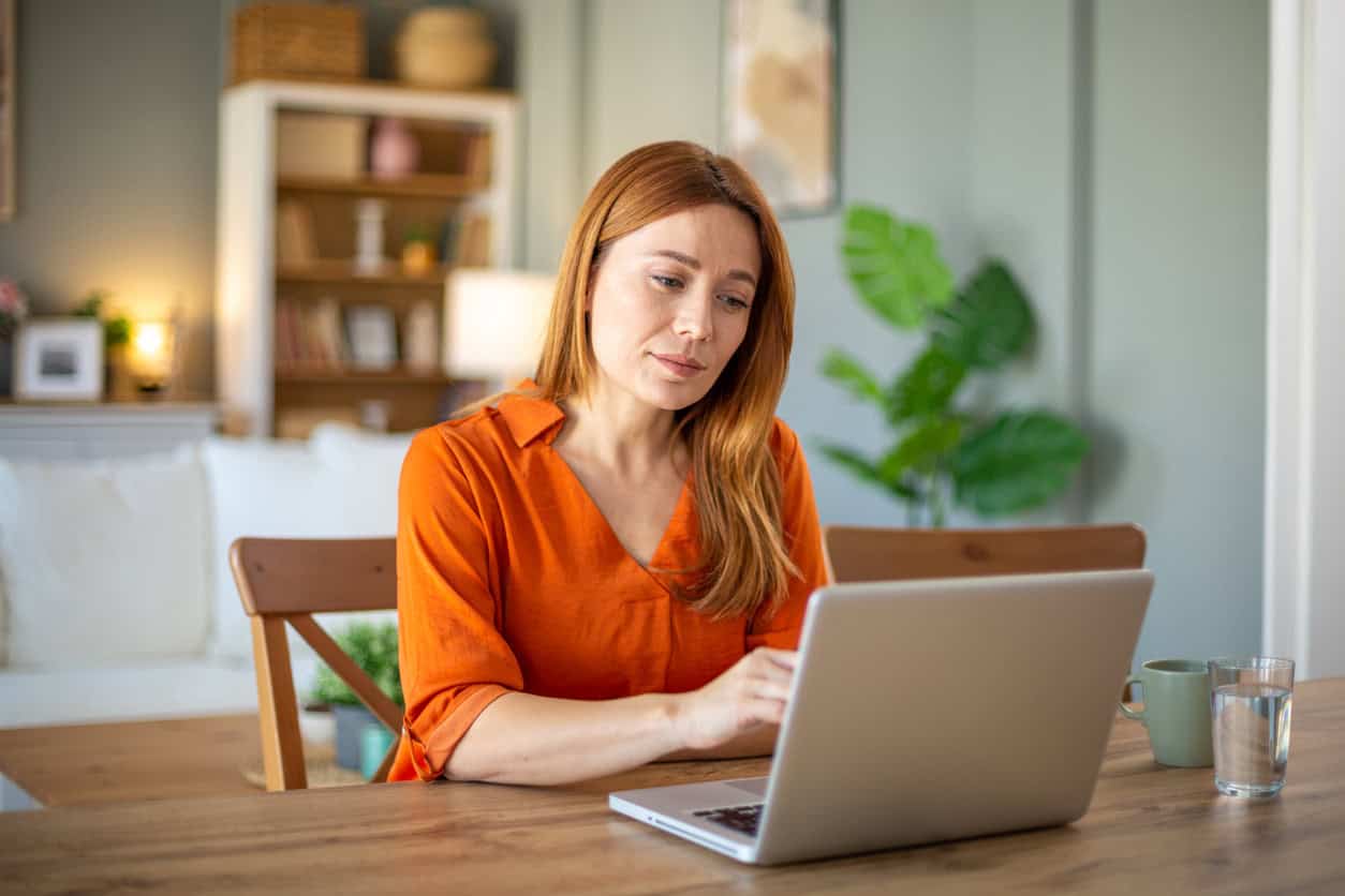 Woman managing finances on laptop at home, planning how to meet credit card minimum spend without overspending