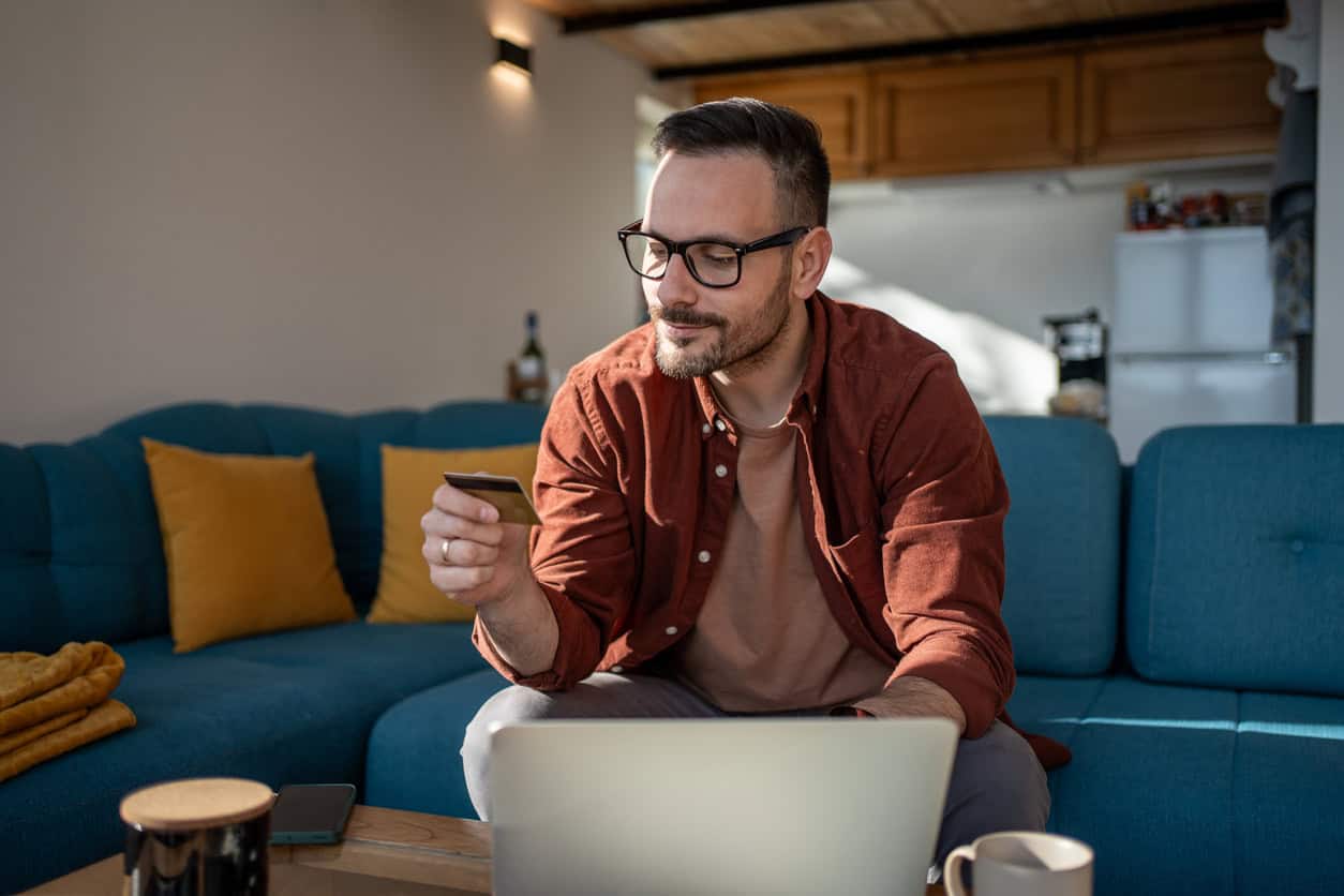 Man at home using laptop and credit card, reading good news about a gold credit card offer