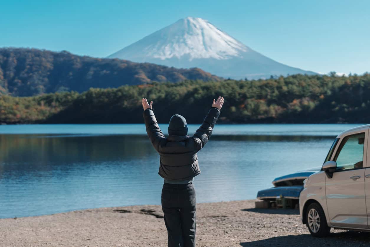 Traveler raising arms by lakeside with Mount Fuji in background on a clear day in Japan