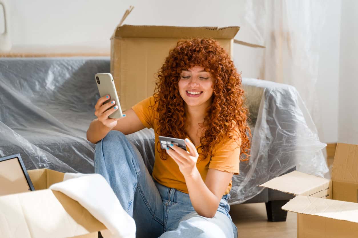 Woman using a credit card and phone to pay rent online while earning reward points in a new home