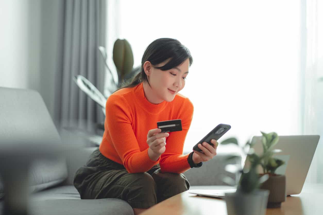 Woman using a credit card and mobile phone to pay rent online from home