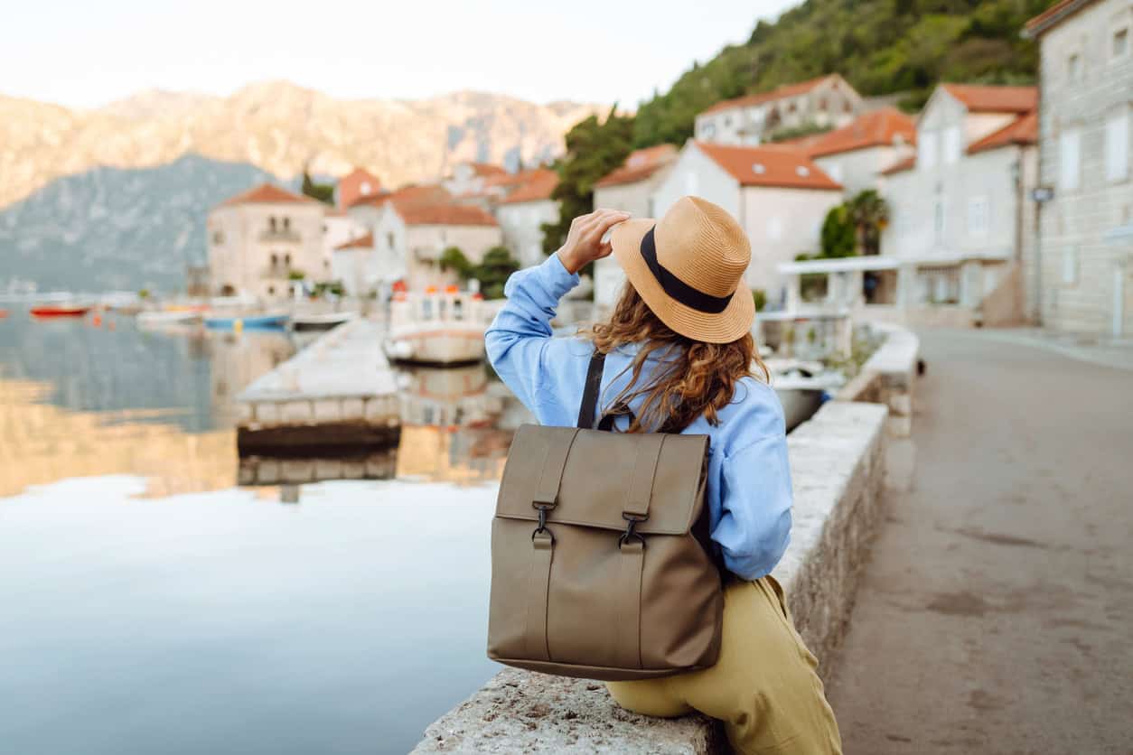 Solo female traveler with backpack and hat enjoying scenic coastal European village by the water