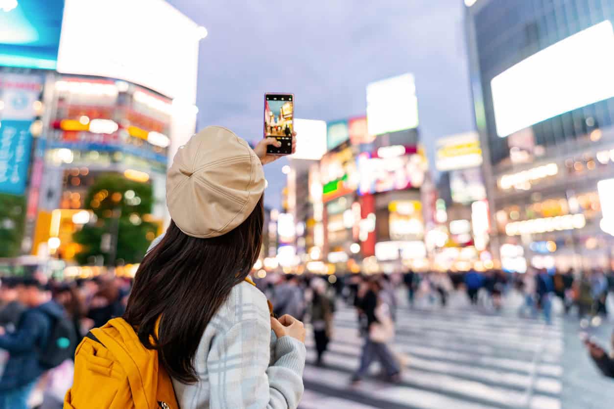 Traveler taking photo at Shibuya Crossing in Tokyo at night with bright city lights and crowds
