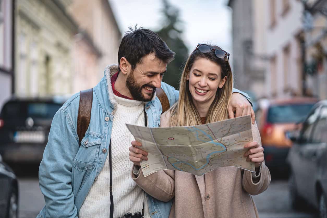 Smiling couple of tourists standing on a city street while reading a paper map during a trip abroad