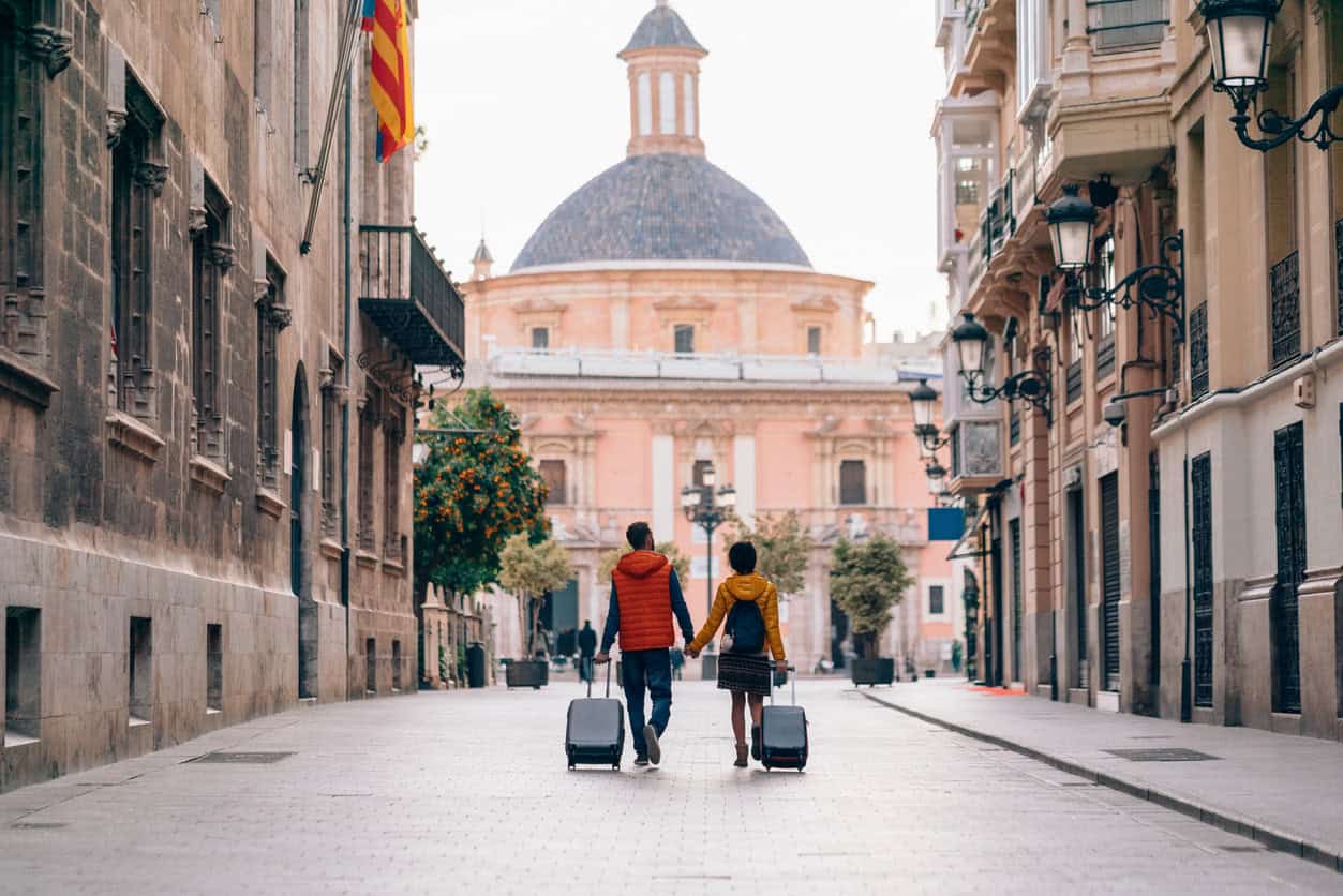 Couple walking through a European city street with luggage, enjoying a trip booked with points and miles