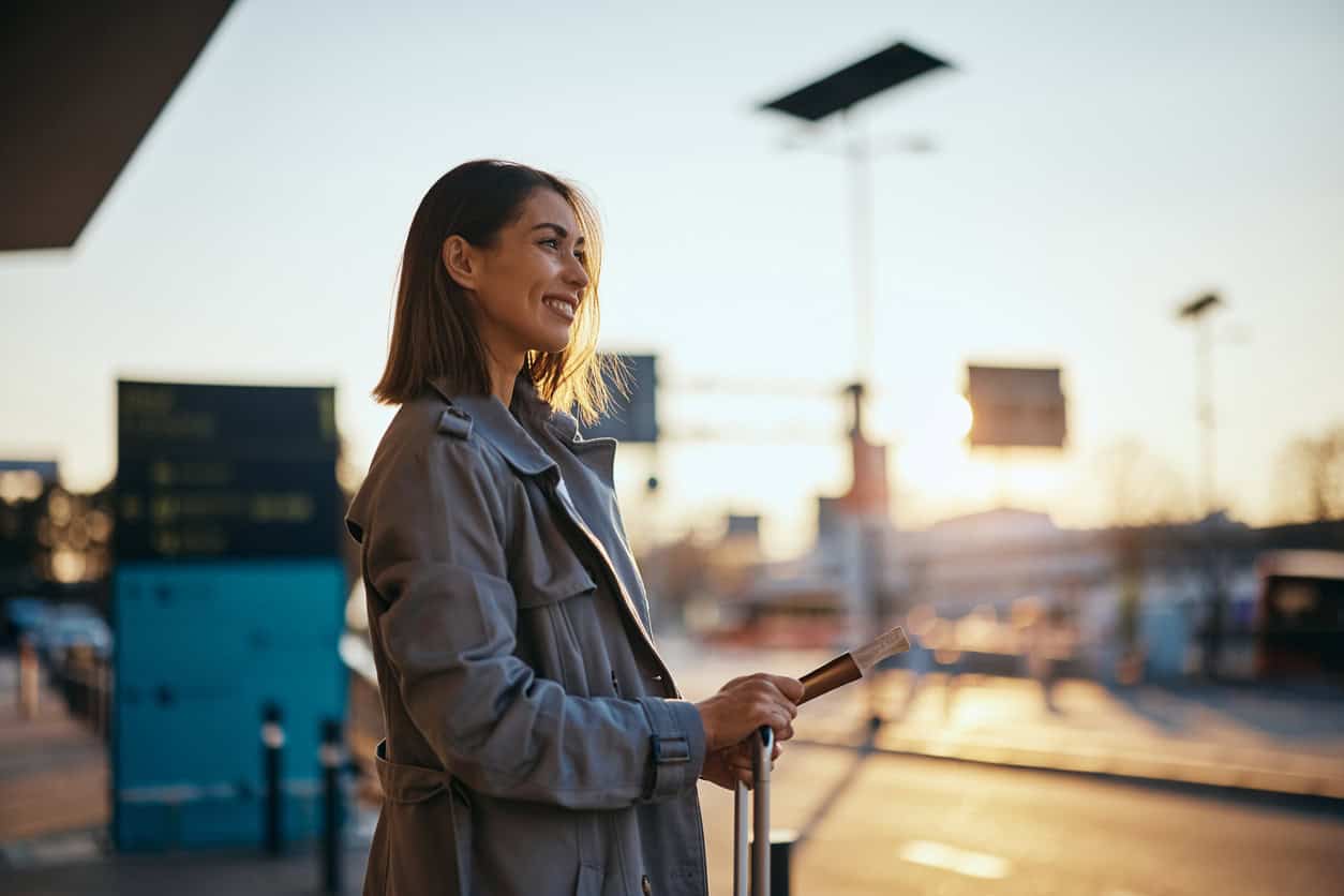 Woman holding a boarding pass and suitcase at an airport during sunrise