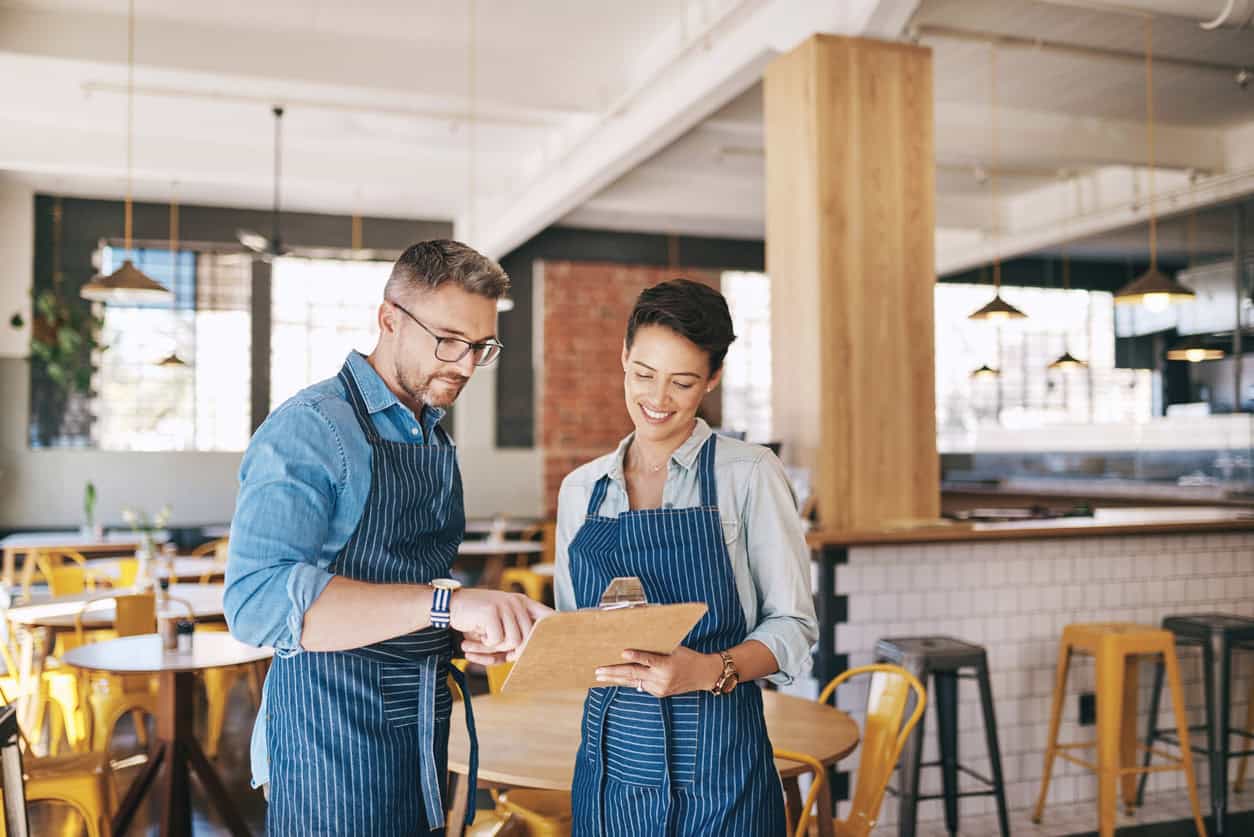 Small business owners reviewing expenses and finances inside a cafe while managing daily business operations