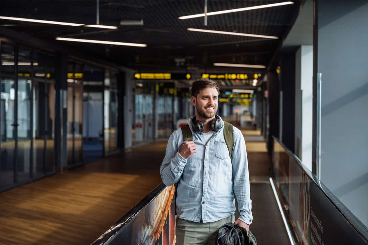 Male traveler walking through an airport terminal with headphones and backpack