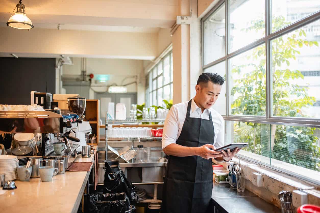 Small business owner in a café using a tablet to manage orders and daily operations