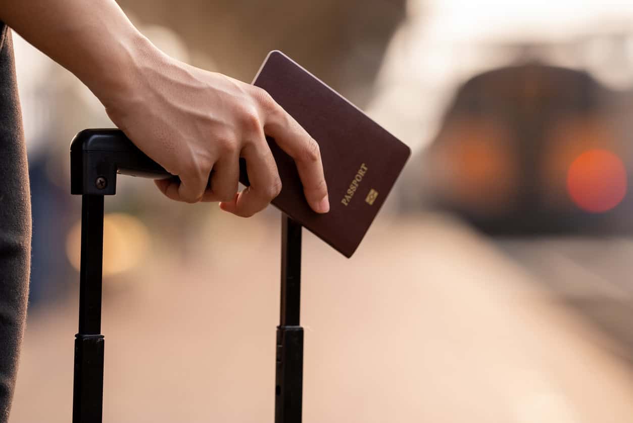 Close-up of a traveler holding a passport and rolling suitcase while waiting at a train or airport platform