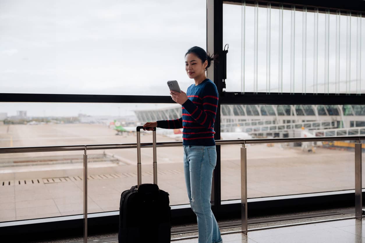 Traveler standing in an airport terminal with a suitcase while checking a smartphone before a flight