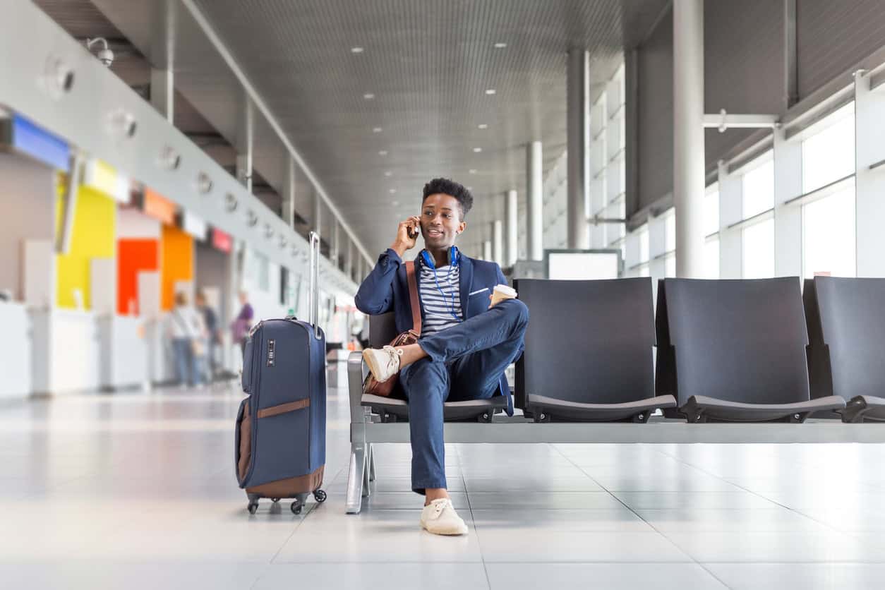 Traveler sitting in an airport terminal with a suitcase while talking on the phone before a flight