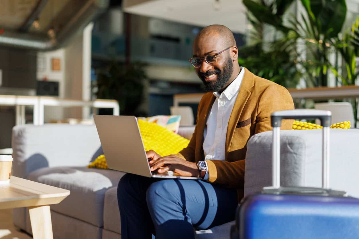 Business traveler working on a laptop in an airport lounge with carry-on luggage nearby