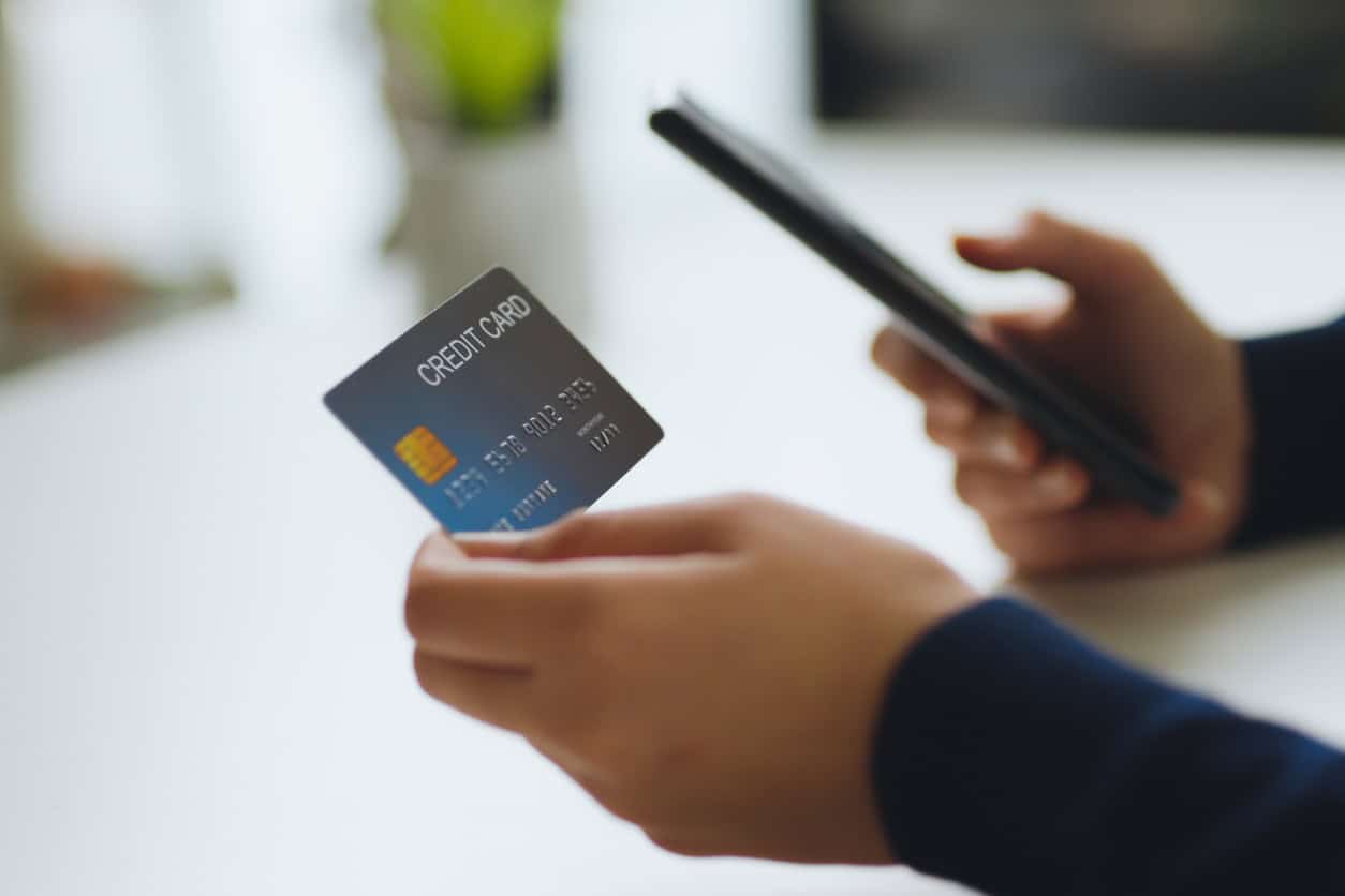 Person holding a credit card and smartphone while making an online purchase.