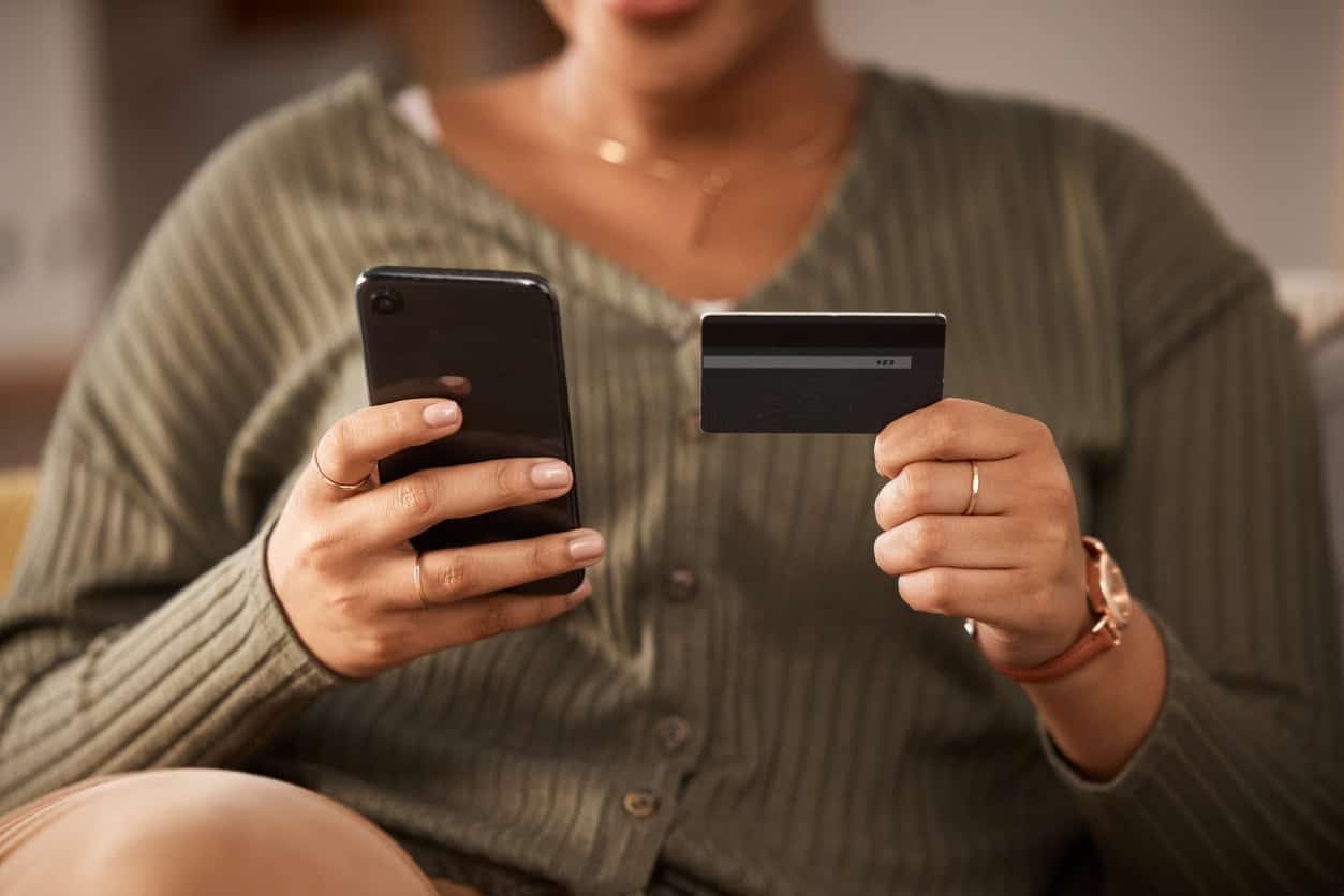 Person comparing credit card features and benefits on a smartphone while holding a credit card.
