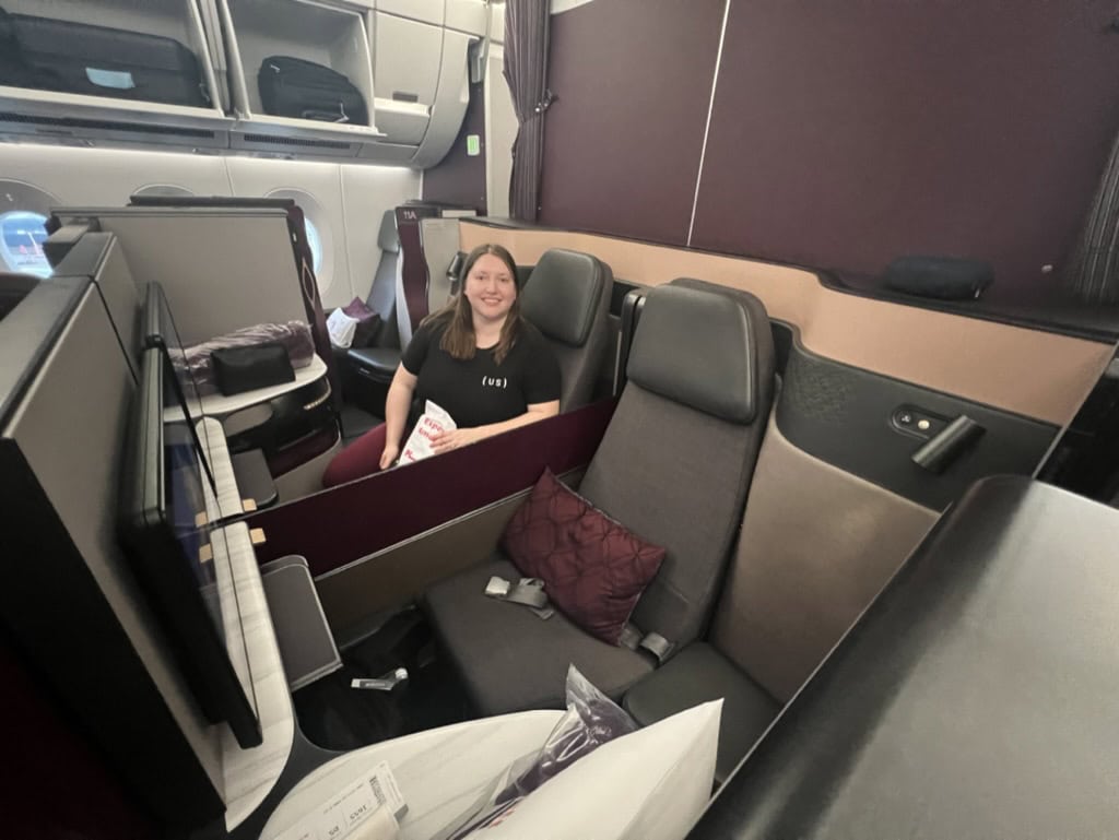 Passenger seated in a Qatar Airways Qsuite business class cabin, showcasing the spacious suite-style seating that can be booked using Chase Ultimate Rewards points transferred to airline partners.