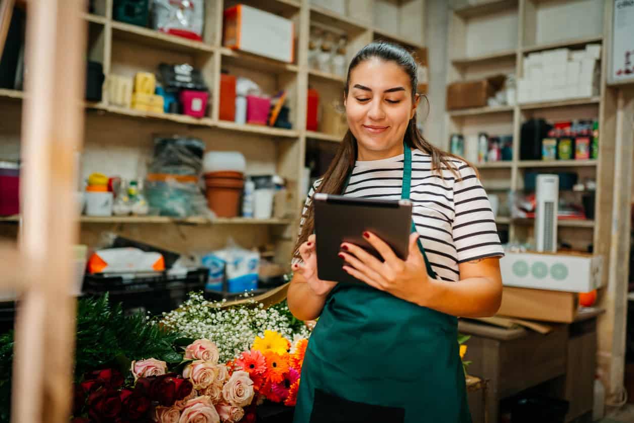 Small business owner using a tablet to manage inventory and daily operations in a flower shop.