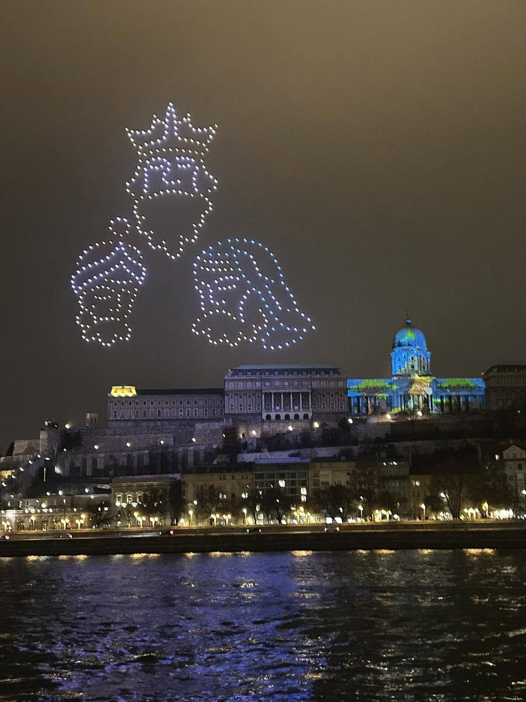 Drone light show above the Hungarian National Gallery and Buda Castle, viewed from the Danube River during a nighttime cruise in Budapest.
