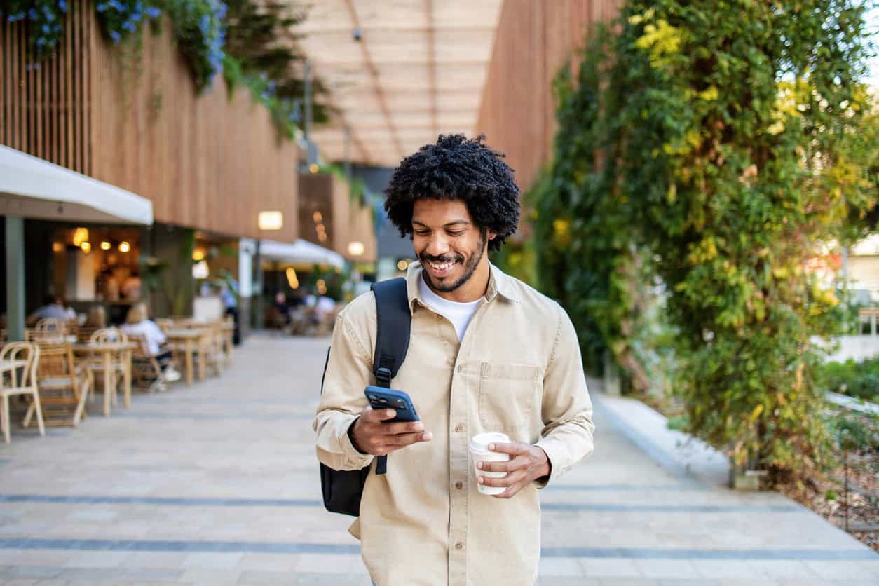 Traveler checking a mobile phone while walking outdoors, comparing credit card benefits and statement credits to offset an annual fee.