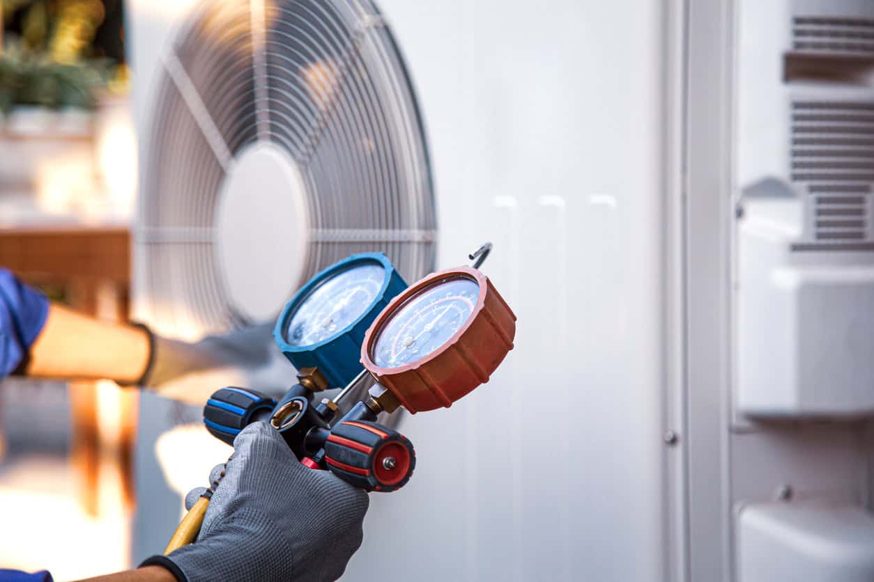 HVAC technician using manifold gauges to service an outdoor air conditioning unit.