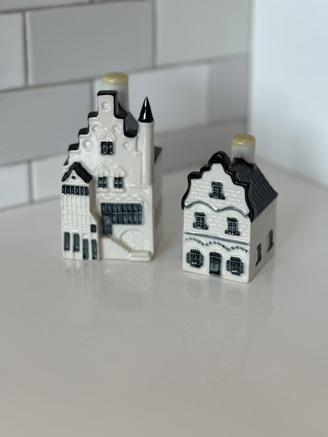 Two KLM Delft Blue miniature houses displayed side by side, including House 101 and the commemorative House 1 anniversary edition, collectible souvenirs traditionally filled with Dutch jenever.