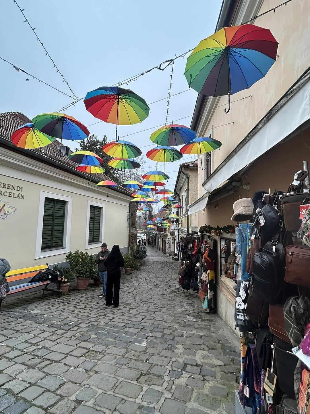 Colorful umbrellas suspended above a cobblestone street in Szentendre, Hungary, an artist village known for its galleries, shops, and charming historic streets.