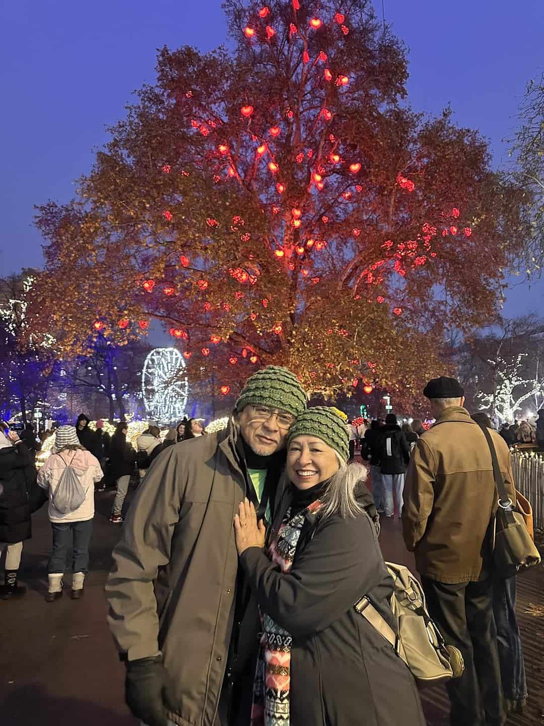 Visitors posing beneath the illuminated Heart Tree at the Vienna Christmas Dream Christmas Market in Rathausplatz, with festive lights and holiday decorations surrounding City Hall.