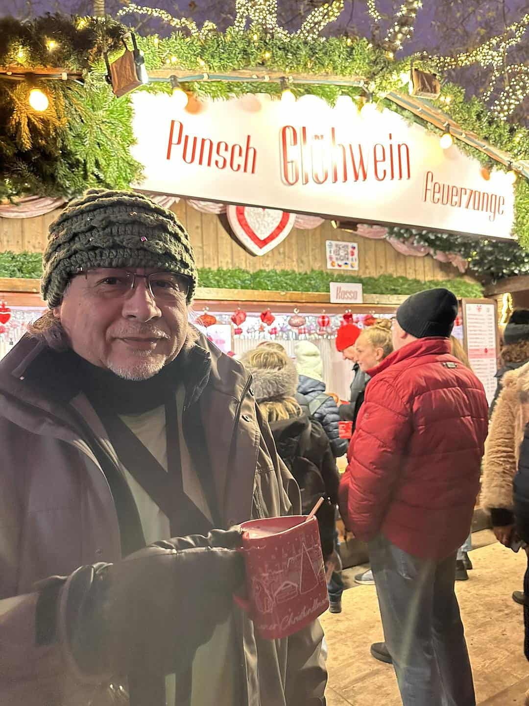 Traveler holding a collectible heart-shaped Vienna Christmas market mug filled with Glühwein in front of a festive drink stand at the Vienna Christmas Dream on Rathausplatz.