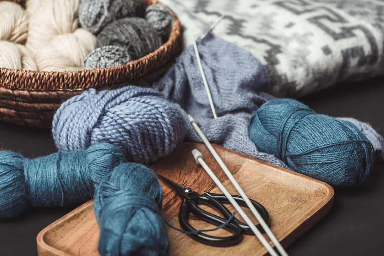 Colorful skeins of yarn, knitting needles, scissors, and a partially completed knitting project.