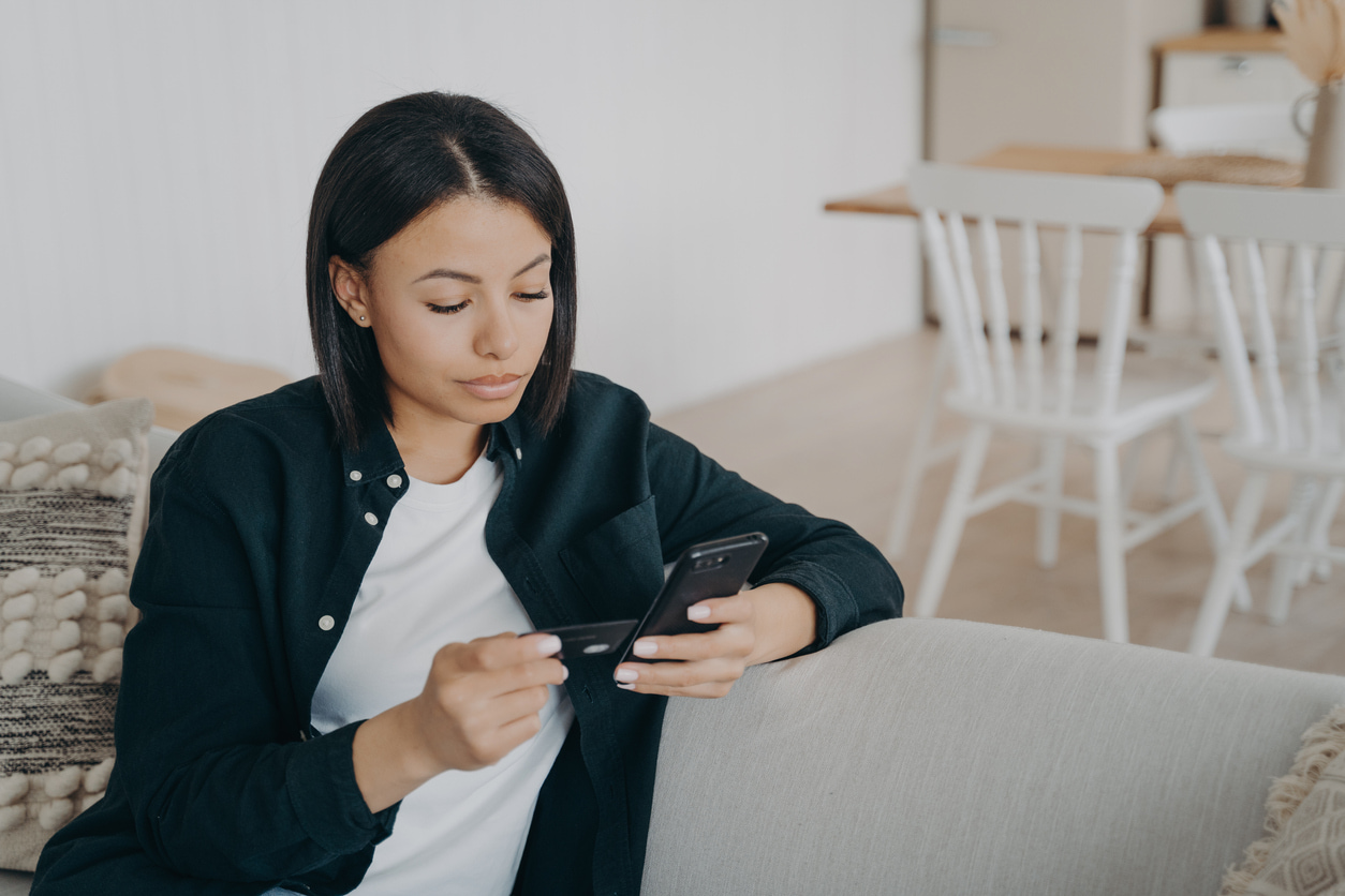 Woman using a smartphone while holding a credit card at home.