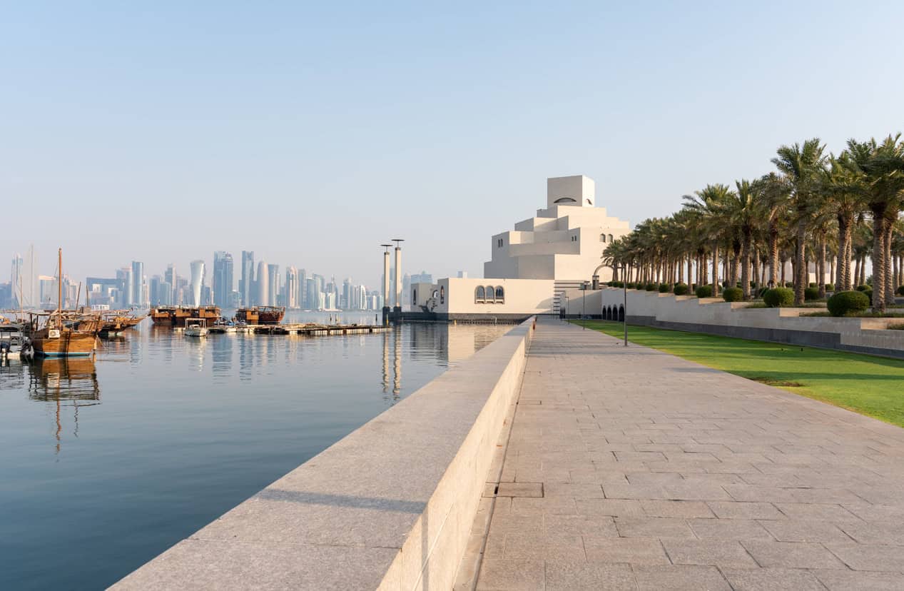 Waterfront view of Doha, Qatar, featuring the Museum of Islamic Art, traditional dhow boats and the city skyline.