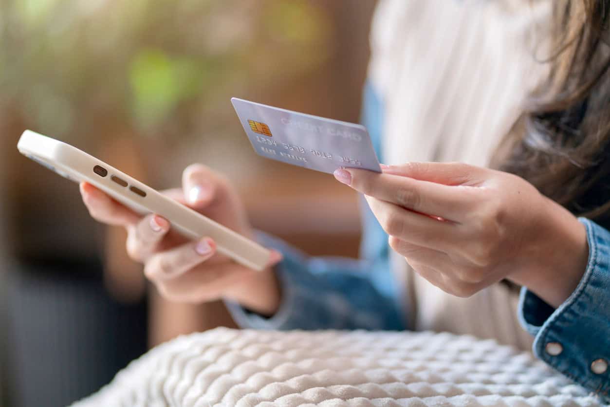 Person holding a credit card and smartphone, representing mobile payments and everyday credit card spending.