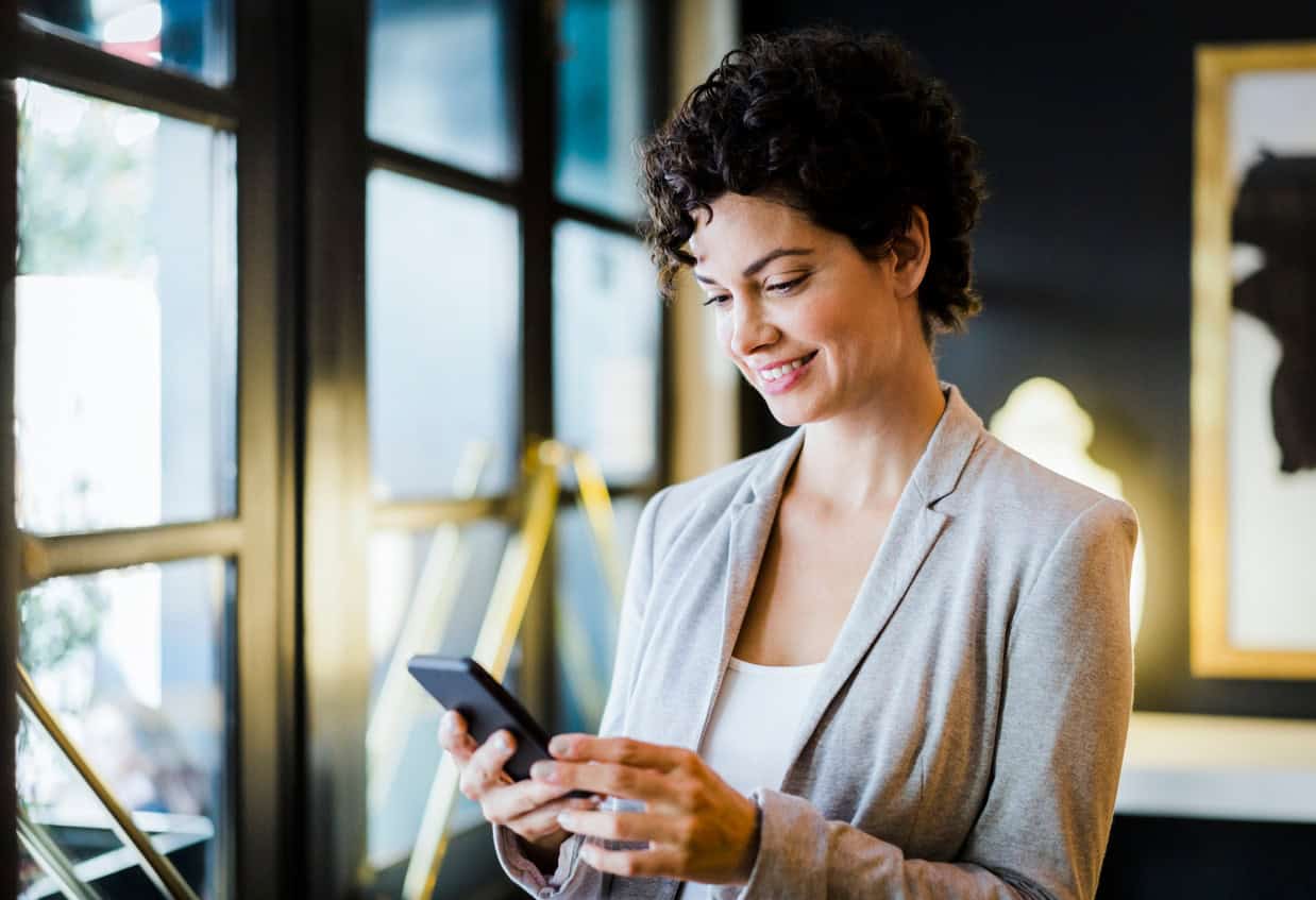 Businesswoman using a smartphone while standing in a modern office or workspace.