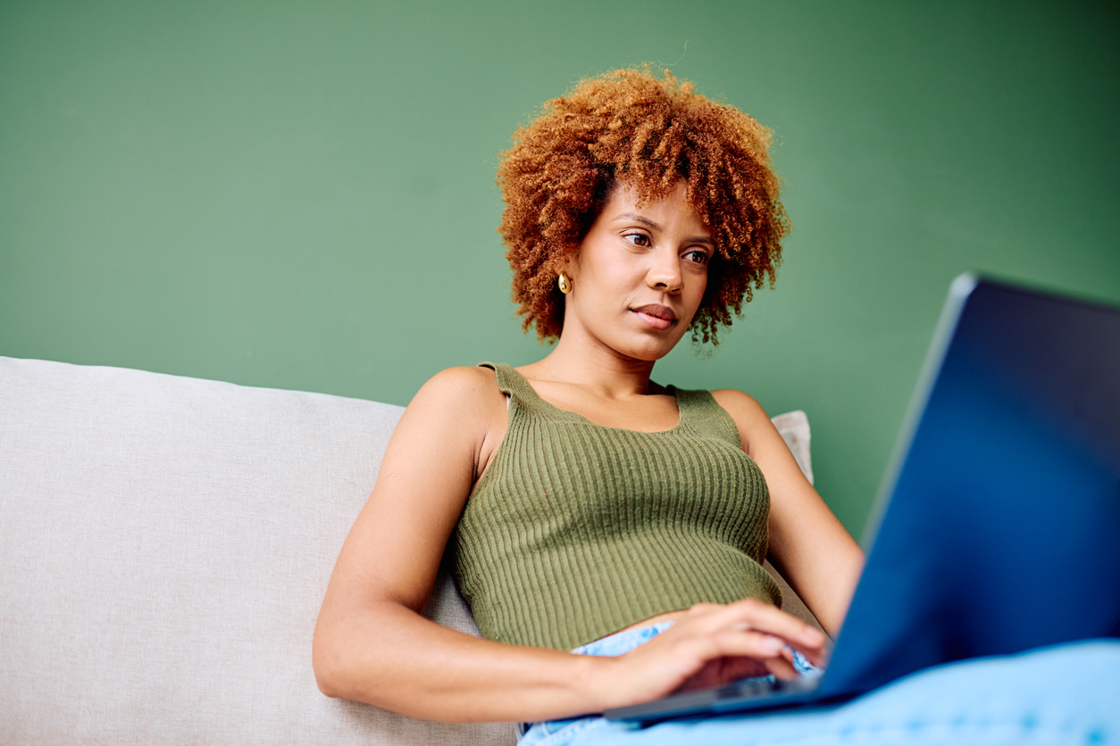 Woman checking credit card news on a laptop while sitting comfortably on a sofa at home.