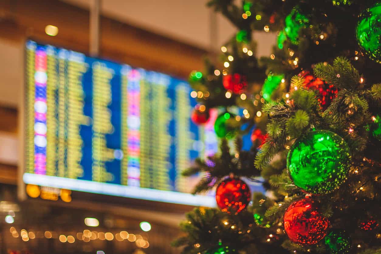 Christmas tree with colorful ornaments in front of an airport departures board.