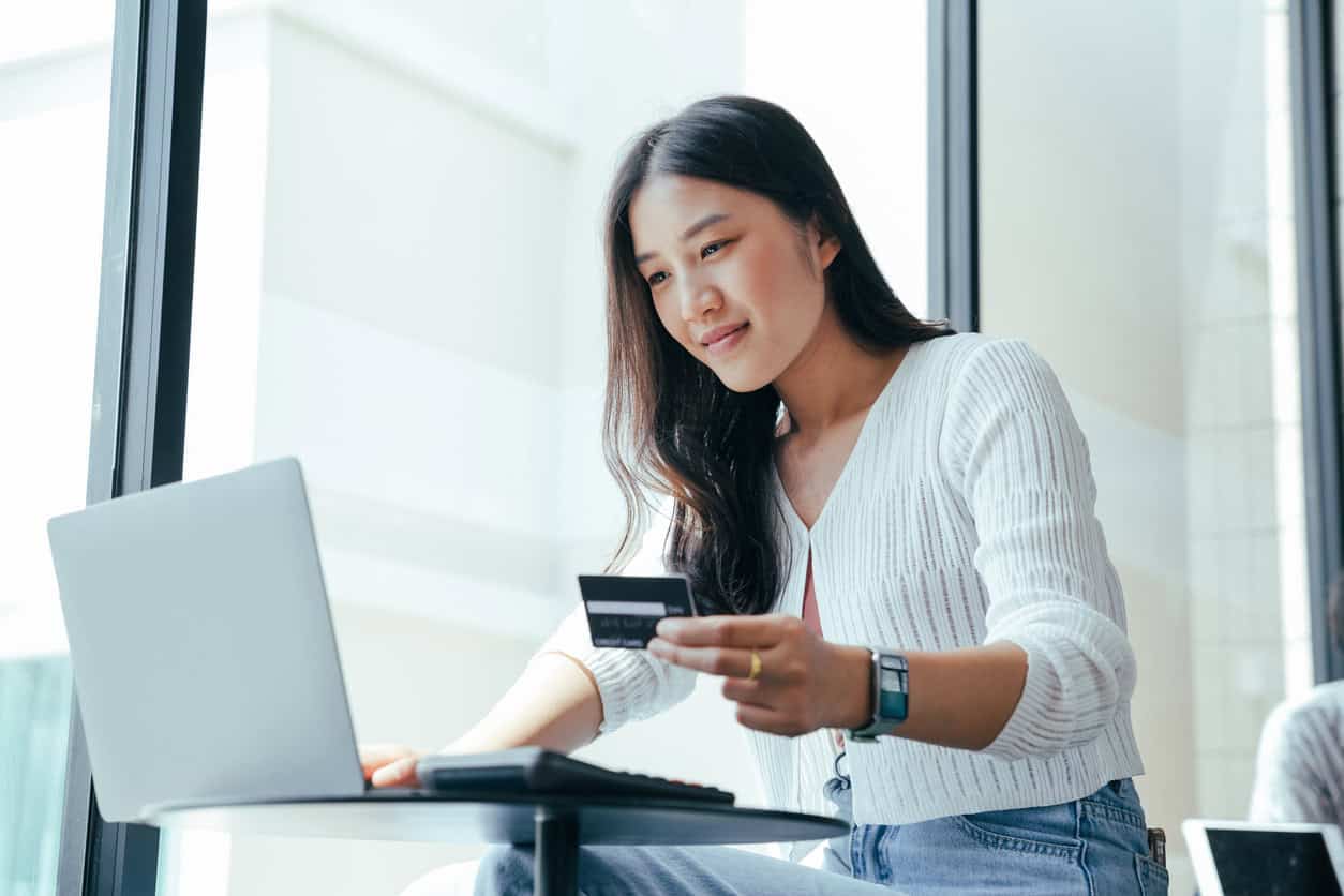 Woman using a laptop while holding a credit card, representing online travel booking and credit card payments.