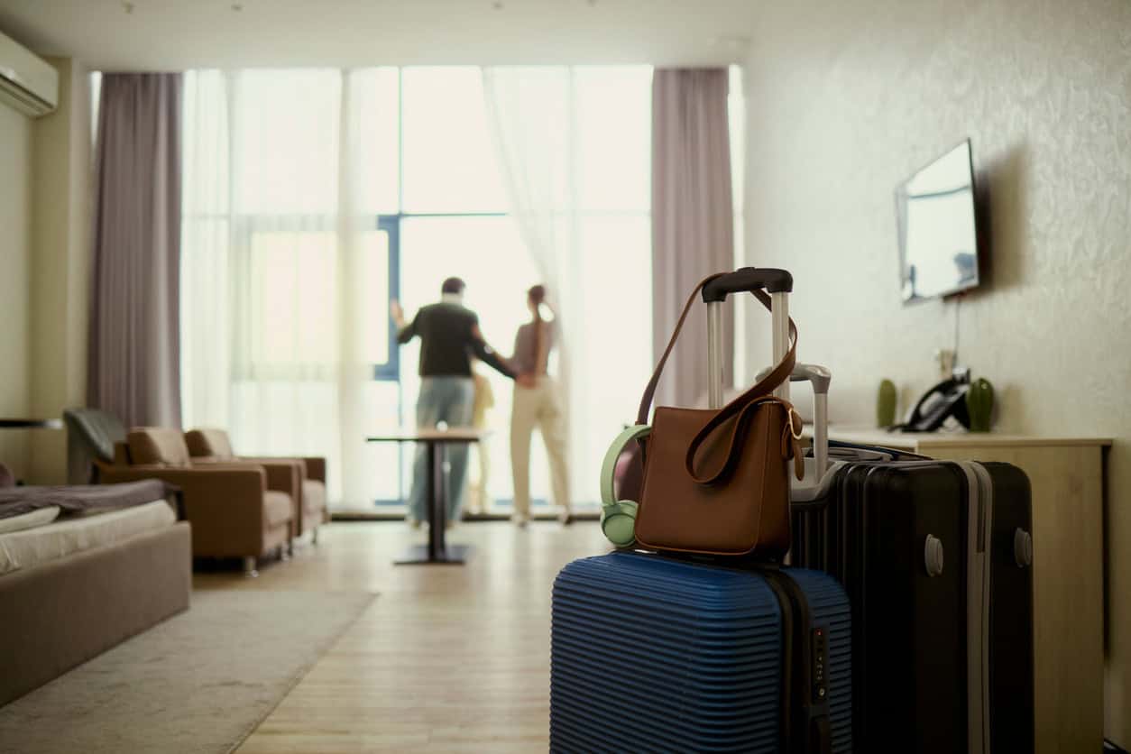 Hotel room with packed luggage, travel bags, and a couple near the window, representing a hotel stay during a trip.