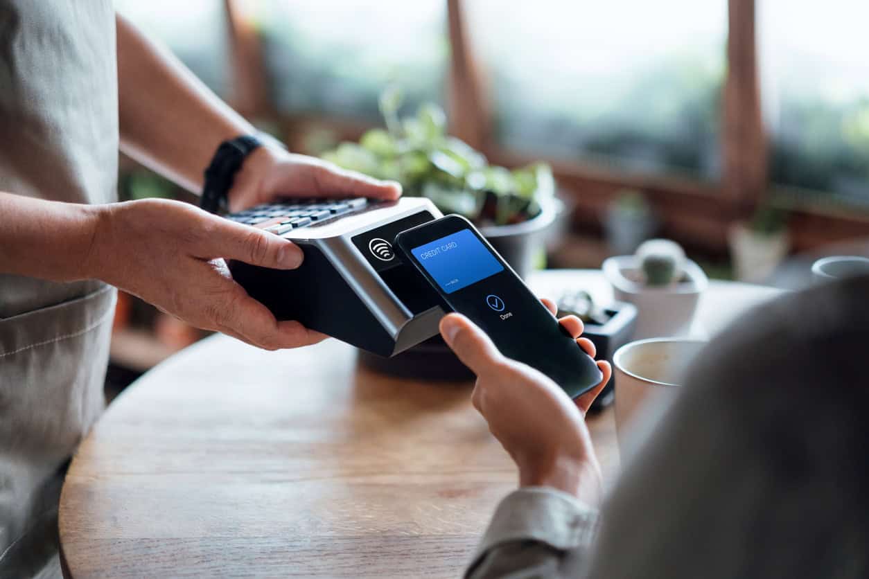 Customer using a contactless credit card terminal at a café, representing credit card spending and payments.
