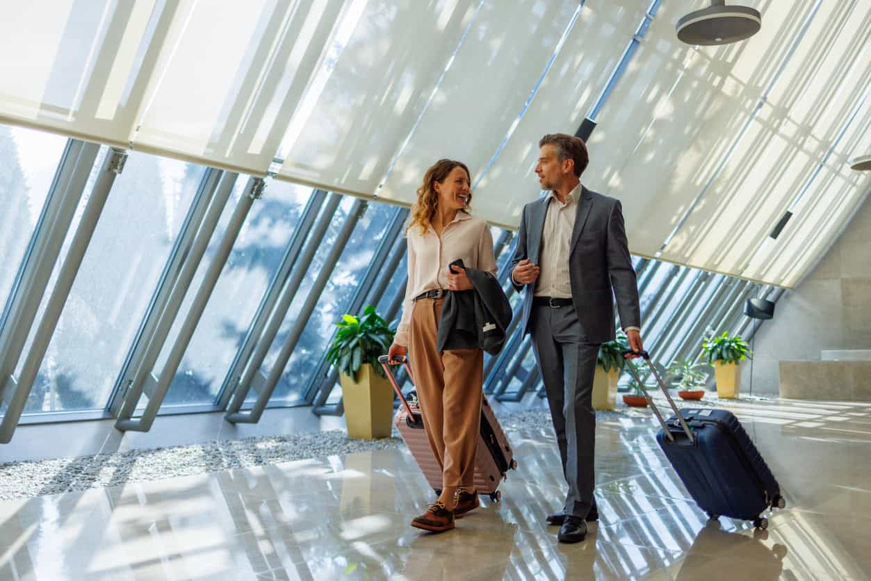 Business travelers walking through an airport terminal with rolling suitcases.