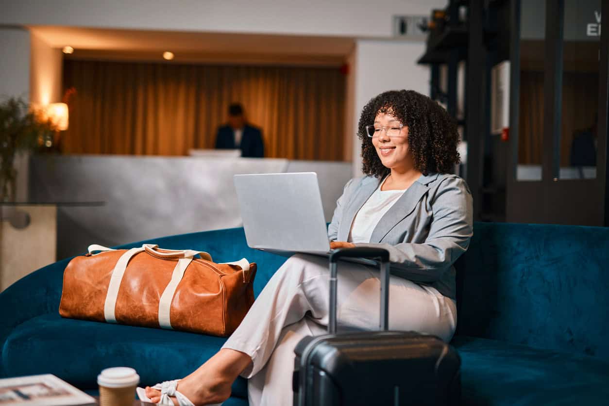 Woman reviewing information on a laptop while relaxing in a hotel lounge with her luggage.