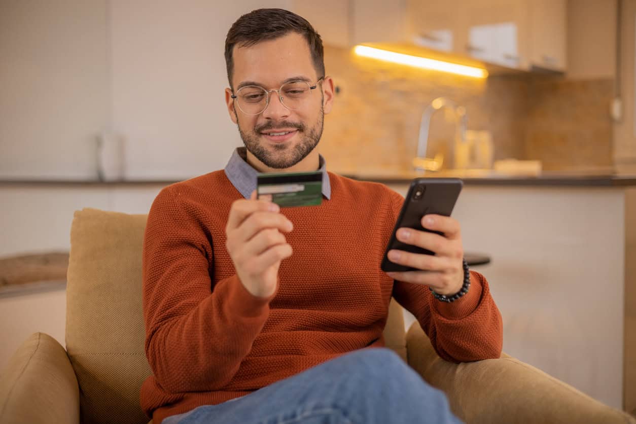 Man reviewing a credit card while using a smartphone at home.