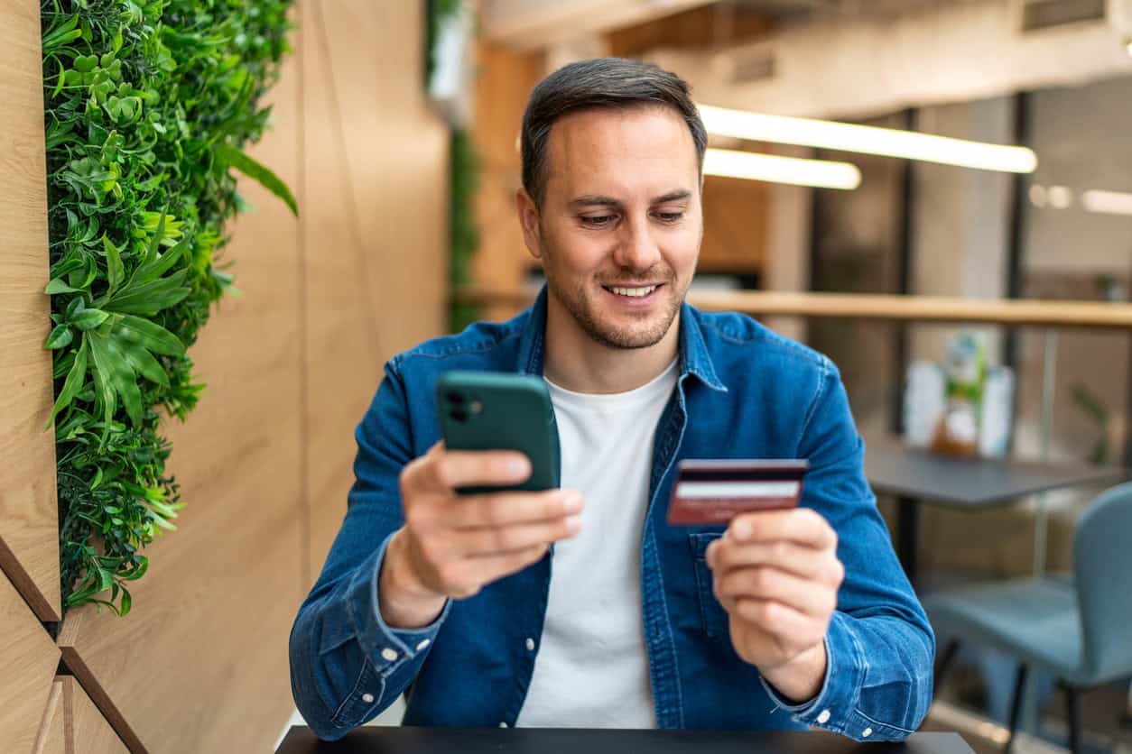 Man smiling while using a smartphone and holding a credit card while shopping online.