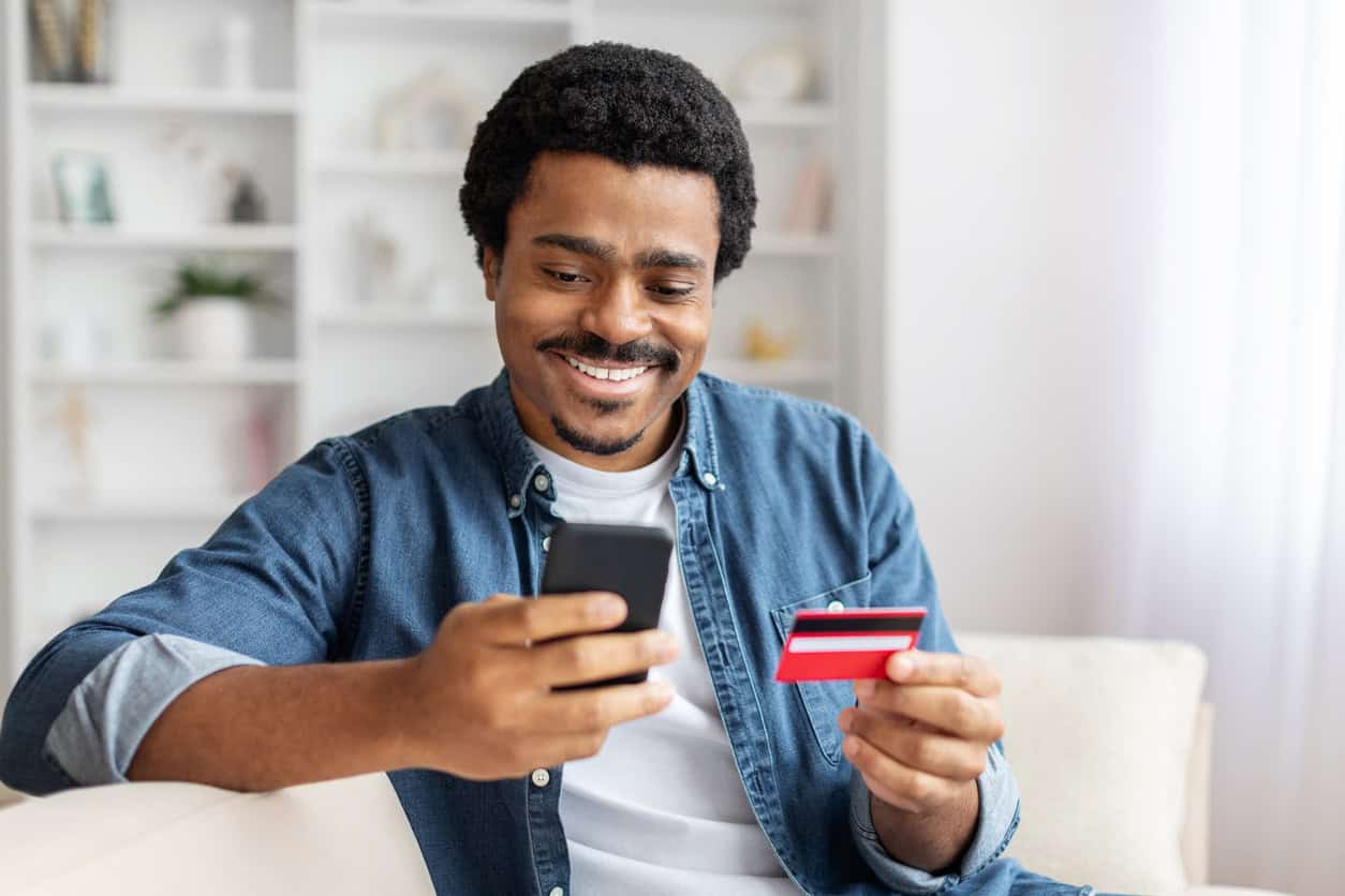 Man holding a credit card while using a smartphone to shop online.