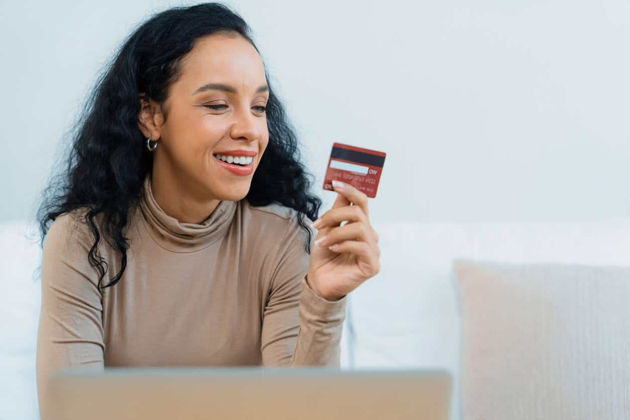 Woman smiling while holding a credit card and shopping online on a laptop.